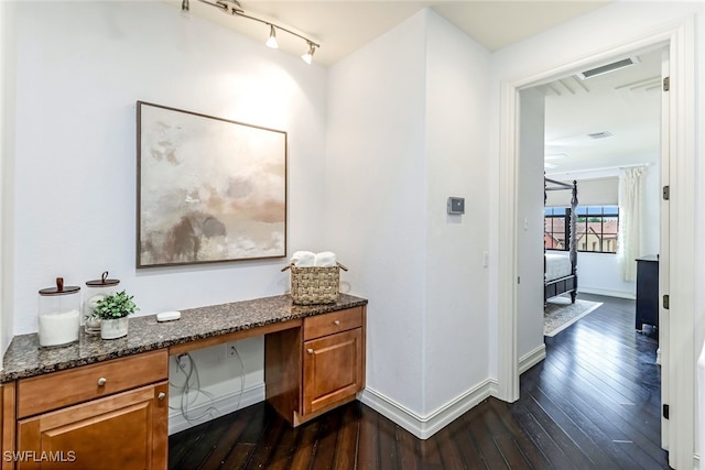 hall featuring track lighting, dark wood-style flooring, visible vents, and baseboards