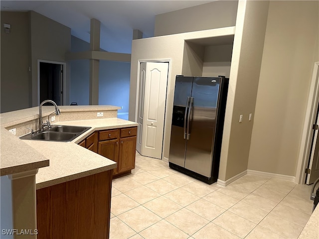 kitchen with lofted ceiling, sink, light tile patterned floors, kitchen peninsula, and stainless steel refrigerator with ice dispenser