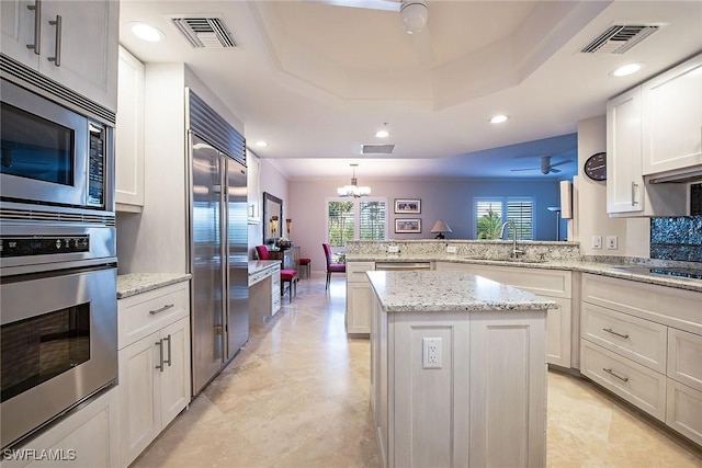 8473 Bay Colony Dr Unit 203, Naples, FL 34108 - kitchen featuring built in appliances, a center island, a tray ceiling, sink, and white cabinetry