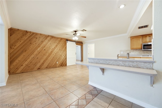 kitchen with crown molding, tasteful backsplash, a kitchen bar, a barn door, and wood walls