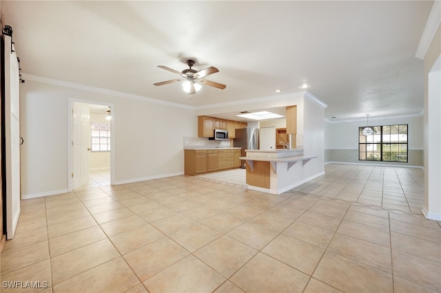 kitchen with a breakfast bar, appliances with stainless steel finishes, ornamental molding, a barn door, and kitchen peninsula