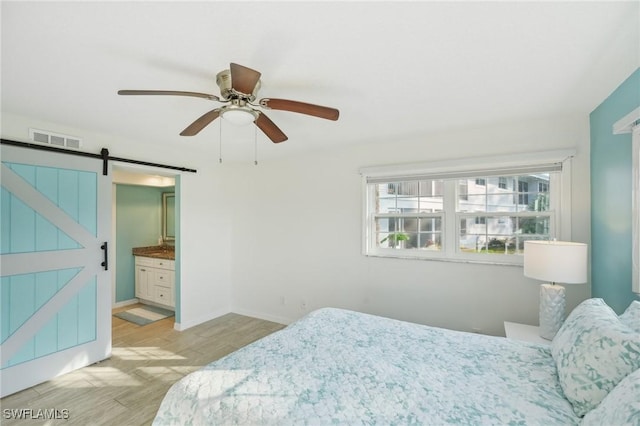 bedroom with ensuite bathroom, a barn door, ceiling fan, and light hardwood / wood-style flooring