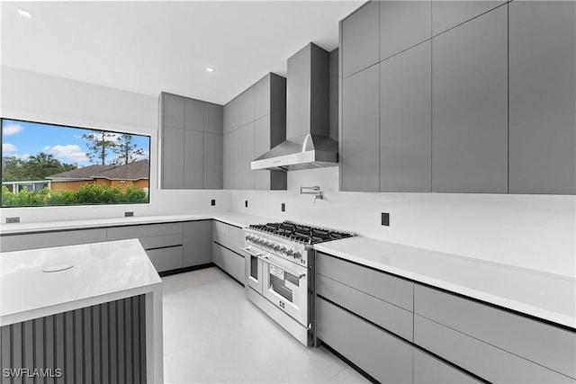 kitchen with range with two ovens, gray cabinetry, and wall chimney exhaust hood