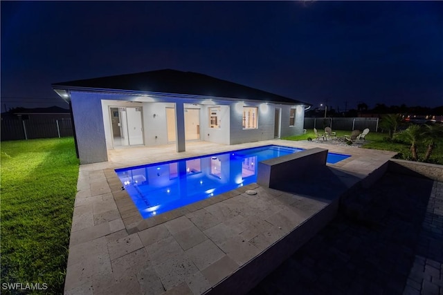 pool at night with a yard and a patio area