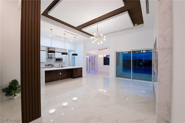 kitchen featuring sink, hanging light fixtures, stainless steel appliances, a notable chandelier, and wall chimney exhaust hood