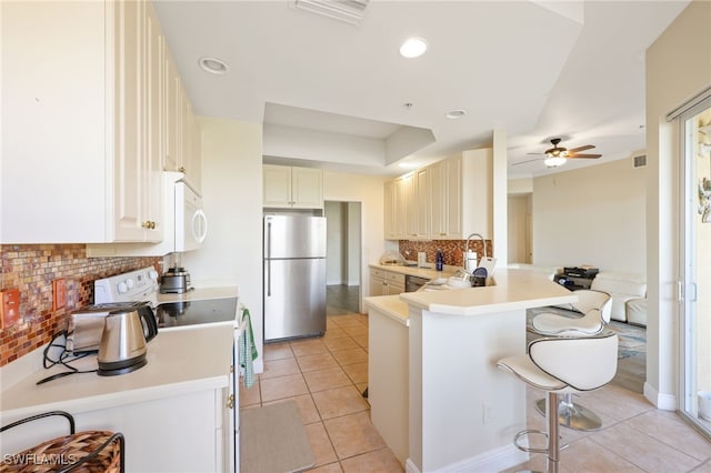 kitchen with a breakfast bar area, range, light tile patterned floors, stainless steel fridge, and kitchen peninsula