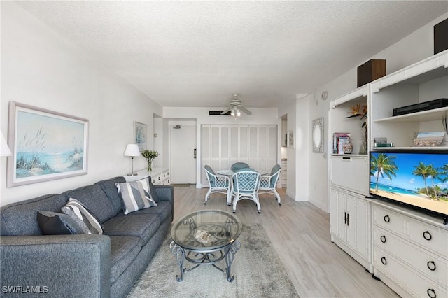 living room with ceiling fan, light hardwood / wood-style flooring, and a textured ceiling