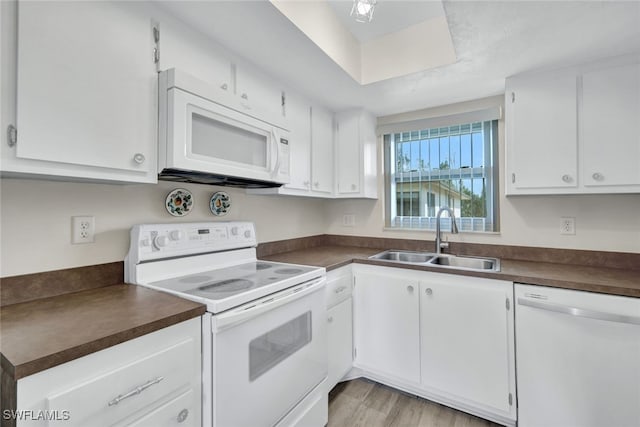 kitchen with dark countertops, white appliances, white cabinets, and a sink