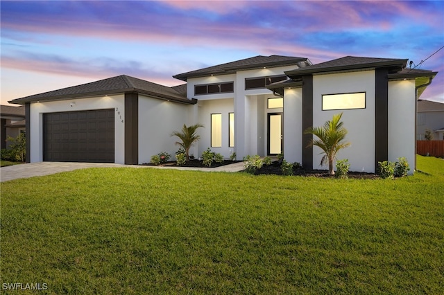 prairie-style home with a garage, concrete driveway, a front yard, and stucco siding