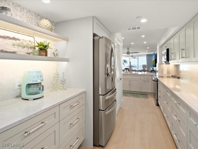 kitchen with light stone countertops, appliances with stainless steel finishes, white cabinets, and ceiling fan