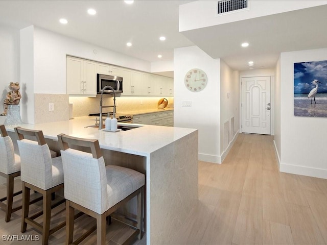 kitchen featuring sink, a breakfast bar area, light hardwood / wood-style flooring, tasteful backsplash, and kitchen peninsula