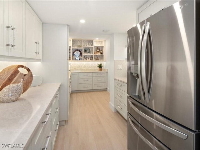 kitchen featuring tasteful backsplash, white cabinetry, light hardwood / wood-style floors, stainless steel refrigerator with ice dispenser, and light stone countertops