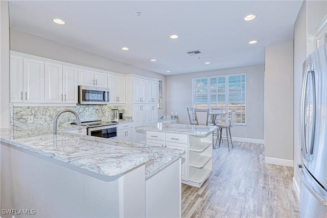 kitchen with stainless steel appliances, light stone countertops, white cabinets, a kitchen island, and kitchen peninsula