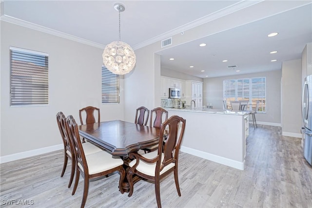 dining area featuring crown molding, sink, and light hardwood / wood-style flooring