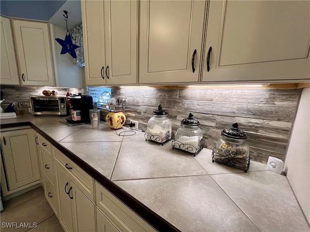 kitchen featuring light tile patterned floors, tile counters, cream cabinetry, and decorative backsplash