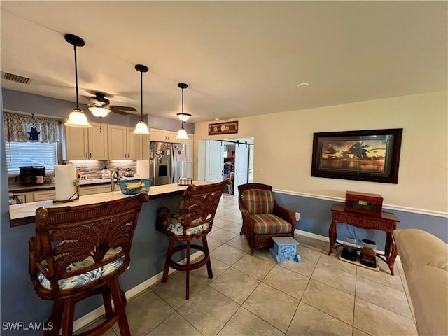 kitchen featuring a breakfast bar area, decorative backsplash, stainless steel fridge with ice dispenser, decorative light fixtures, and a barn door