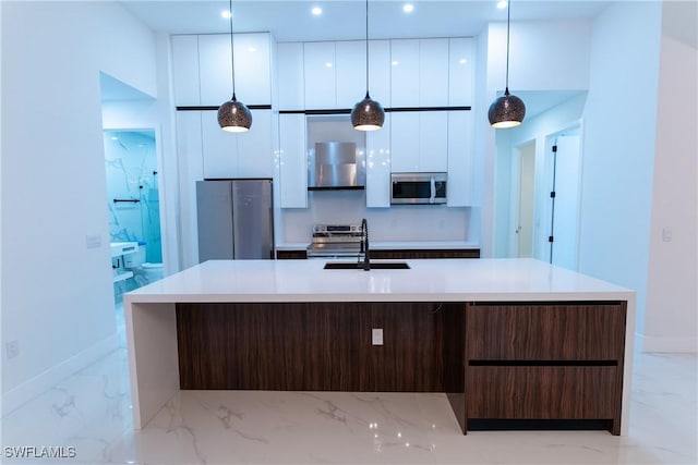 kitchen featuring appliances with stainless steel finishes, white cabinetry, hanging light fixtures, dark brown cabinetry, and a center island with sink