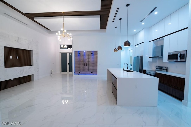 kitchen with pendant lighting, sink, appliances with stainless steel finishes, dark brown cabinetry, and a center island with sink