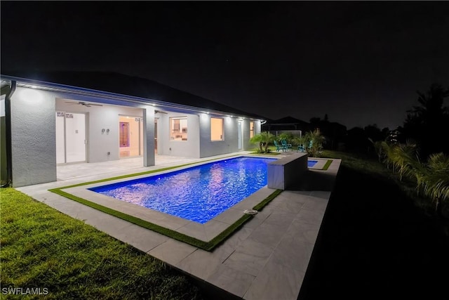 pool at night featuring ceiling fan and a patio