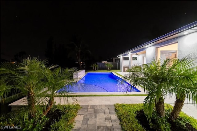 pool at night featuring a patio area