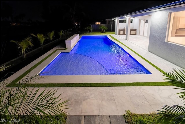 pool at night featuring a patio