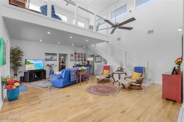 living room with a towering ceiling, light hardwood / wood-style floors, and ceiling fan