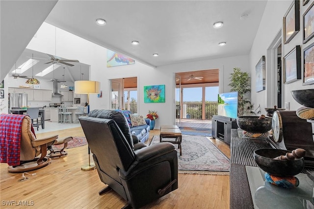 living room featuring ceiling fan, a towering ceiling, light wood-type flooring, and a skylight