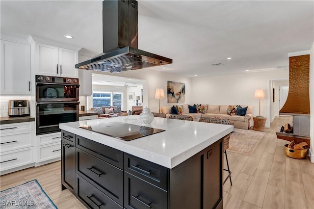 kitchen with white cabinetry, island range hood, light wood-type flooring, a kitchen island, and black appliances