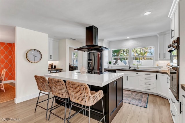 kitchen featuring stainless steel refrigerator with ice dispenser, sink, island range hood, a kitchen island, and white cabinets