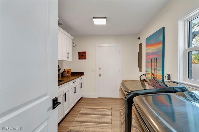 laundry area featuring cabinets, washing machine and clothes dryer, electric panel, and light hardwood / wood-style floors