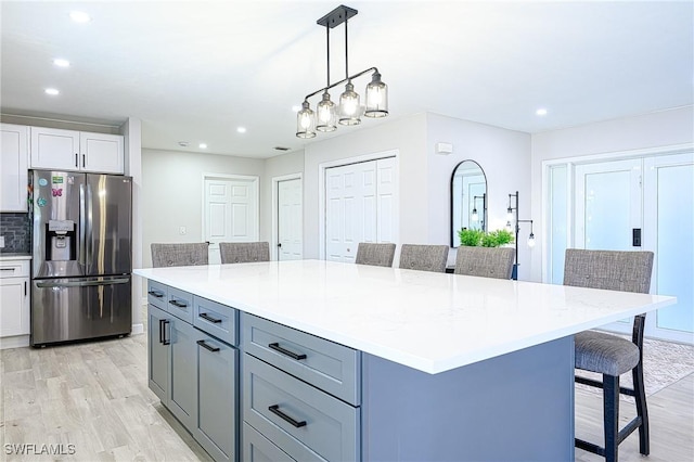 kitchen with a center island, stainless steel fridge with ice dispenser, hanging light fixtures, white cabinets, and a kitchen bar