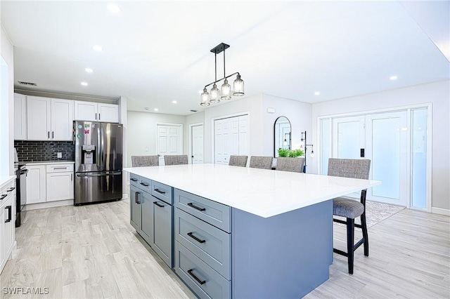 kitchen featuring decorative light fixtures, white cabinetry, a breakfast bar area, stainless steel fridge, and a center island