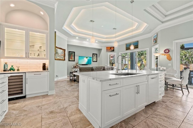 kitchen with sink, a kitchen island with sink, white cabinetry, a tray ceiling, and beverage cooler