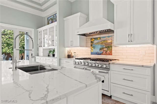 kitchen with light stone counters, wall chimney range hood, white cabinetry, and double oven range