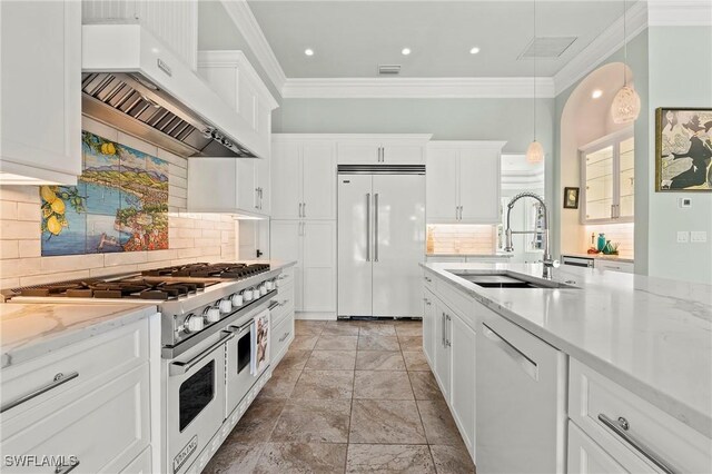 kitchen with wall chimney exhaust hood, sink, white cabinetry, hanging light fixtures, and premium appliances