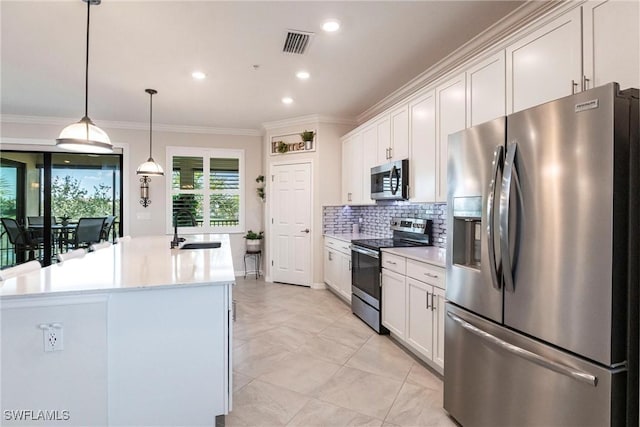 kitchen with appliances with stainless steel finishes, white cabinetry, sink, hanging light fixtures, and a center island with sink