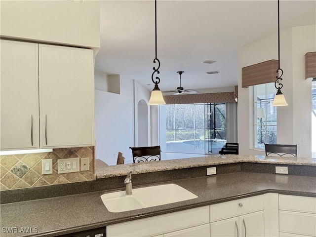 kitchen with hanging light fixtures, sink, white cabinets, and decorative backsplash