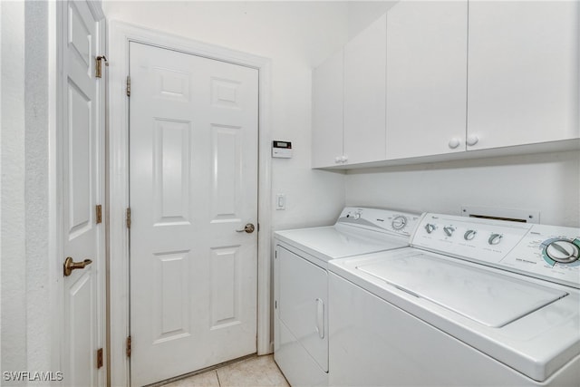 clothes washing area with cabinets, washing machine and clothes dryer, and light tile patterned flooring