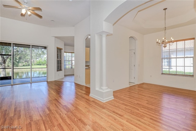 unfurnished living room featuring ceiling fan with notable chandelier, a tray ceiling, decorative columns, and light hardwood / wood-style flooring