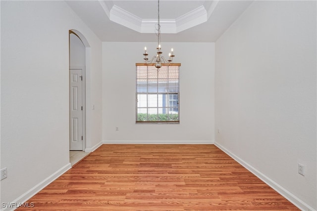 spare room with crown molding, a notable chandelier, a tray ceiling, and light wood-type flooring