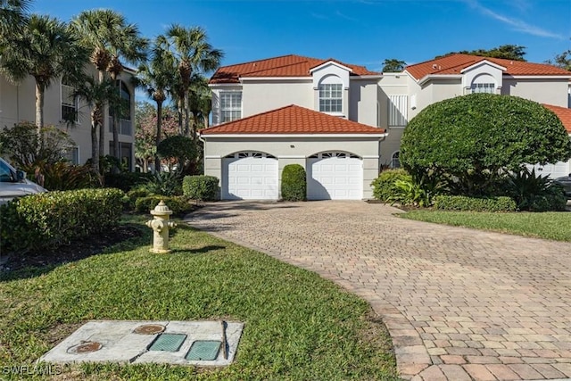 mediterranean / spanish home featuring a garage, a tiled roof, decorative driveway, a front yard, and stucco siding