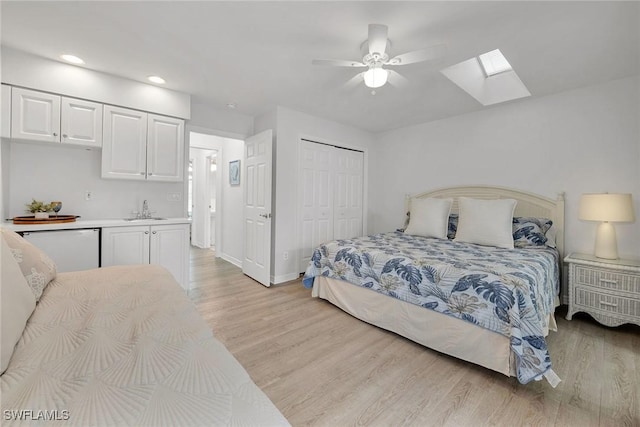 bedroom featuring a closet, sink, a skylight, light hardwood / wood-style floors, and ceiling fan