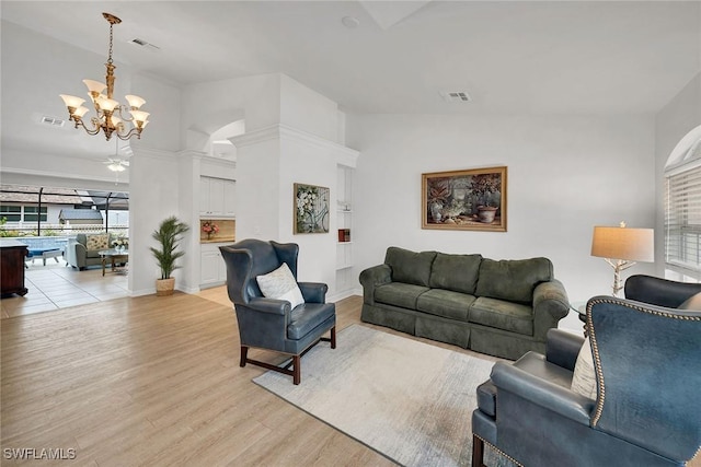 living room with a notable chandelier, light wood-type flooring, a wealth of natural light, and lofted ceiling