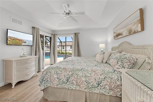 bedroom featuring a tray ceiling, ceiling fan, light wood-type flooring, and access to outside