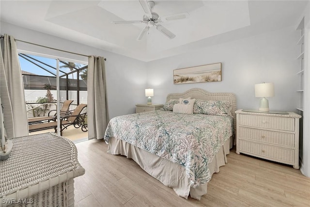 bedroom featuring light wood-type flooring, a tray ceiling, and access to outside