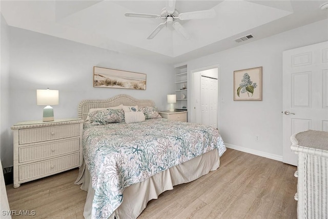 bedroom with a closet, light hardwood / wood-style flooring, ceiling fan, and a raised ceiling