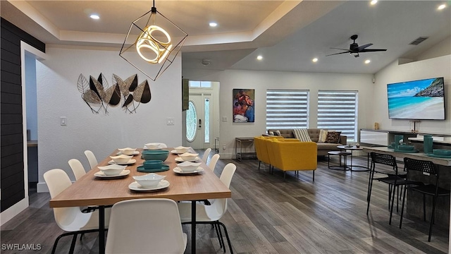 dining area with a tray ceiling, dark hardwood / wood-style flooring, and ceiling fan with notable chandelier