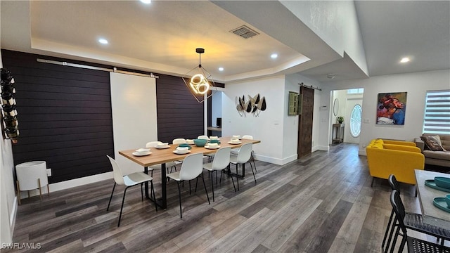 dining room with a barn door, dark wood-type flooring, and a tray ceiling