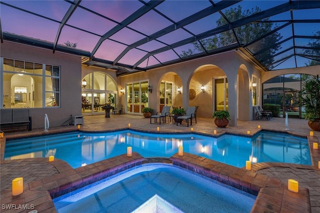 pool at dusk featuring a lanai, a patio area, and an in ground hot tub