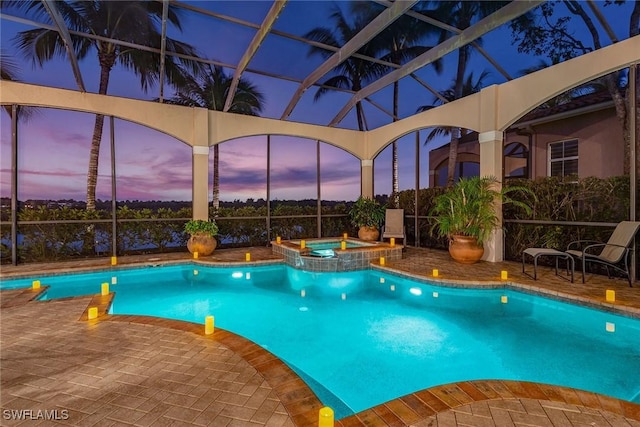 pool at dusk with a lanai, a patio area, and an in ground hot tub